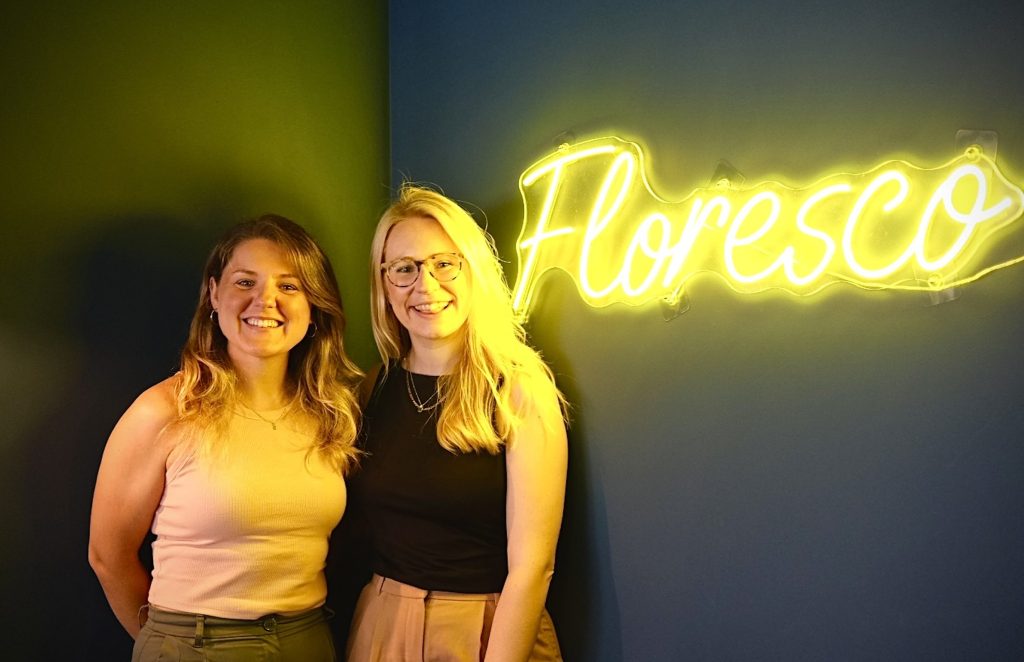Managing Partners Smiling At Camera Next To Neon Sign