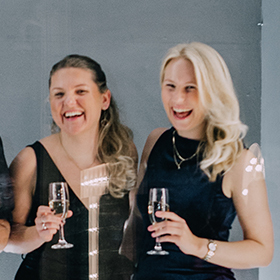 Two women laughing whilst holding champagne flutes