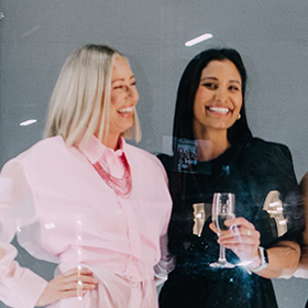 2 women laughing whilst holding champagne flutes
